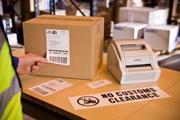 Impresora de etiquetas sobre caja con etiqueta No customs Clearance